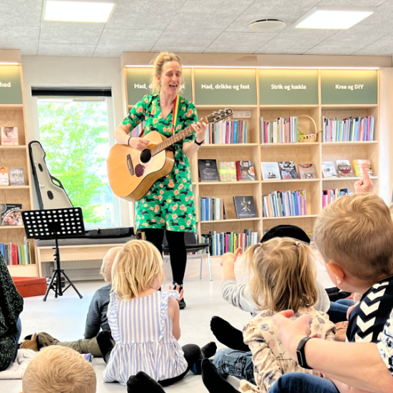 En kvinde med en guitar foran en gruppe børn.