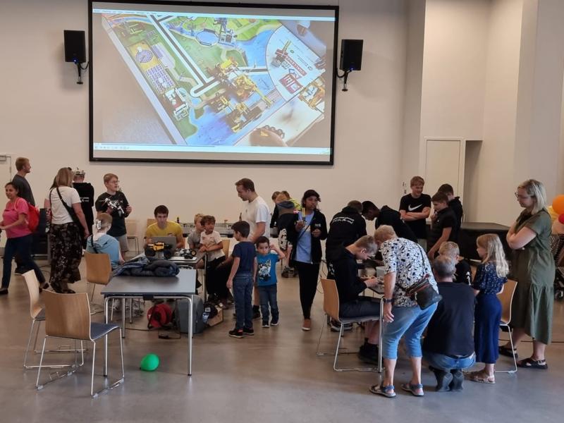 En gruppe mennesker i en sal med LEGO-robotter på borde.