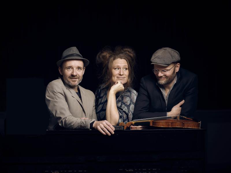 Tre musikere med en violin på en mørk baggrund.